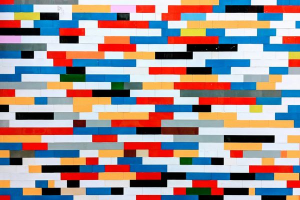 A vibrant mosaic wall constructed from Lego bricks in a spectrum of colors including red, blue, white, yellow, and black, arranged in a modern, geometric pattern